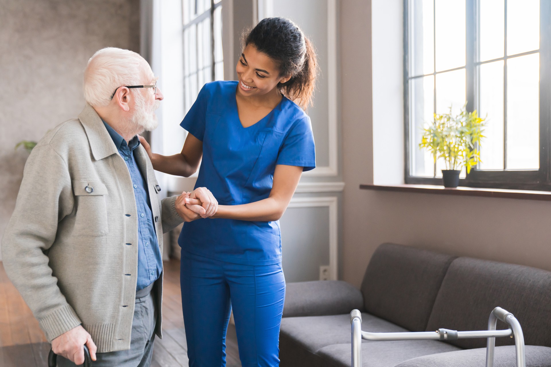 Young caring african nurse helping senior old elderly man grandfather walk . Disable old man trying to walk with the assistance aid of female doctor.